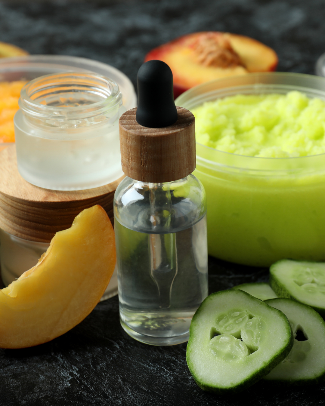 Cosmétiques naturels faits maison : sérum dans un flacon compte-gouttes, crème et gommage à base de concombre et de pêche, ingrédients frais pour des soins visage écologiques.